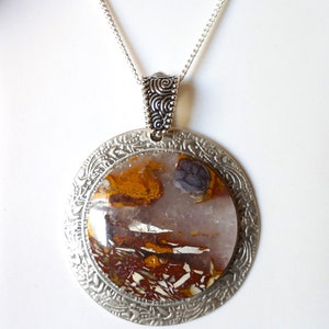 May include: A silver necklace with a round pendant featuring a brown, white and purple agate stone set in a silver filigree frame.