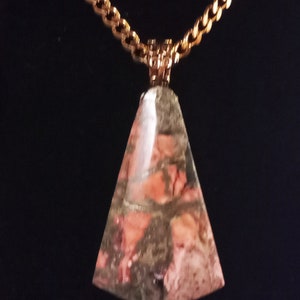 May include: A gold chain necklace with a triangular pendant made of pink and gray patterned stone.