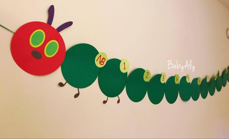 May include: A red and green felt caterpillar banner with the words "Baby Aly" and numbers 1 through 9. The caterpillar has a red head with two large green eyes and a small black nose.