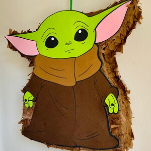 K&ouml;nnte beinhalten: Eine gr&uuml;ne und braune Pi&ntilde;ata in Form einer Figur aus dem Star Wars-Franchise. Die Figur hat gro&szlig;e Ohren, eine braune Robe und ein gr&uuml;nes Gesicht.