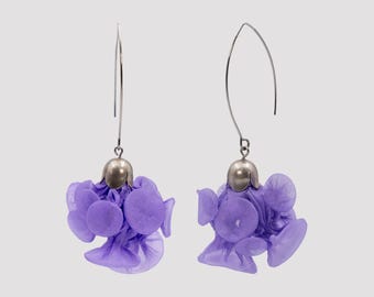 May include: A pair of dangle earrings featuring silver-toned curved ear wires and metallic caps. Each earring is adorned with a cluster of small, circular, light purple fabric petals that create a voluminous, layered, and textured floral appearance.