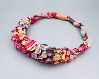 Puede incluir: Un collar colorido hecho de recortes de tela, con una variedad de patrones y colores, incluyendo rosa, rojo, amarillo, azul y verde.