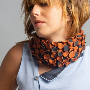 May include: A brown and black fabric necklace with a unique, textured design. The necklace is made of small, round pieces of fabric that are sewn together to create a 3D effect.
