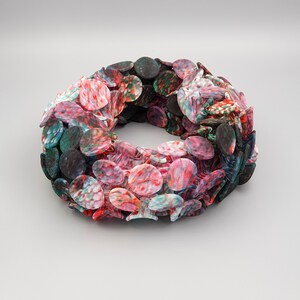 May include: A circular wreath made of colorful, patterned, oval-shaped pieces of fabric. The wreath is made of red, green, and black fabric.