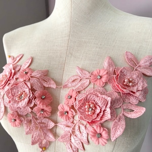 Könnte beinhalten: Rosa florale Spitzenapplikation mit Perlen- und Strassbesatz. Diese zarte Spitzenborte ist perfekt, um jedem Projekt einen Hauch von Eleganz zu verleihen.