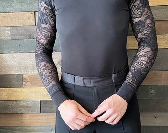May include: A black mock neck shirt with long sleeves featuring a lace pattern on the sleeves. The shirt is paired with black pants.