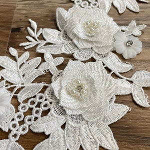 Puede incluir: Borde de encaje blanco con diseños florales y adornos de perlas. El borde presenta hojas y flores delicadas con un efecto 3D en relieve.