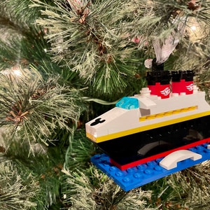 May include: A Lego ornament of the Disney cruise ship, the Disney Magic, with red, white, and blue details. The ornament is hanging on a green Christmas tree.