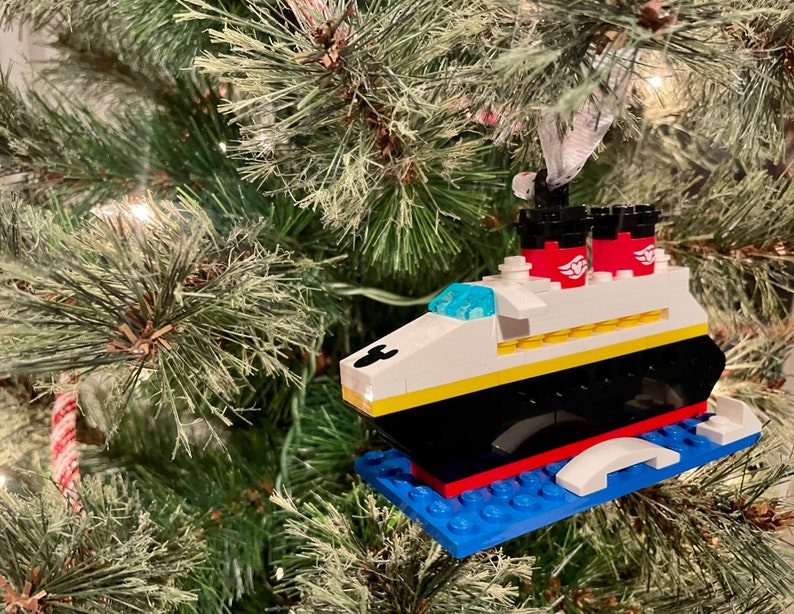 May include: A Lego ornament of the Disney cruise ship, the Disney Magic, with red, white, and blue details. The ornament is hanging on a green Christmas tree.