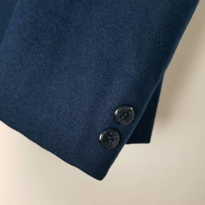 May include: Close-up of the navy blue sleeve of a jacket with two black buttons.
