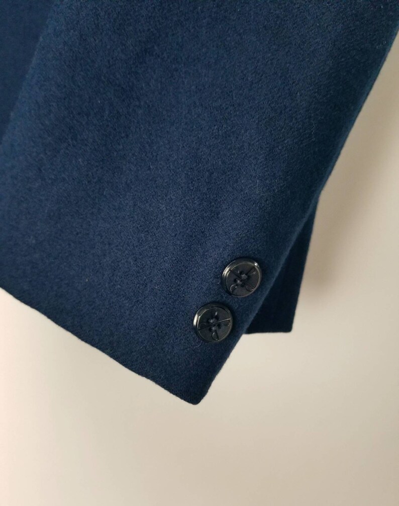 May include: Close-up of the navy blue sleeve of a jacket with two black buttons.
