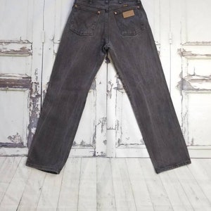May include: A pair of dark gray denim jeans with a brown leather patch on the back pocket that says "Wrangler".