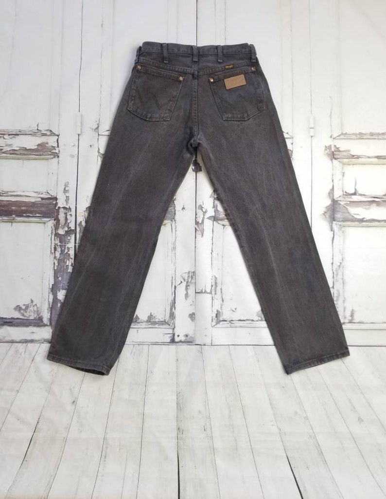 May include: A pair of dark gray denim jeans with a brown leather patch on the back pocket that says "Wrangler".