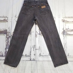 May include: A pair of dark gray denim jeans with a brown leather patch on the back pocket that says "Wrangler".