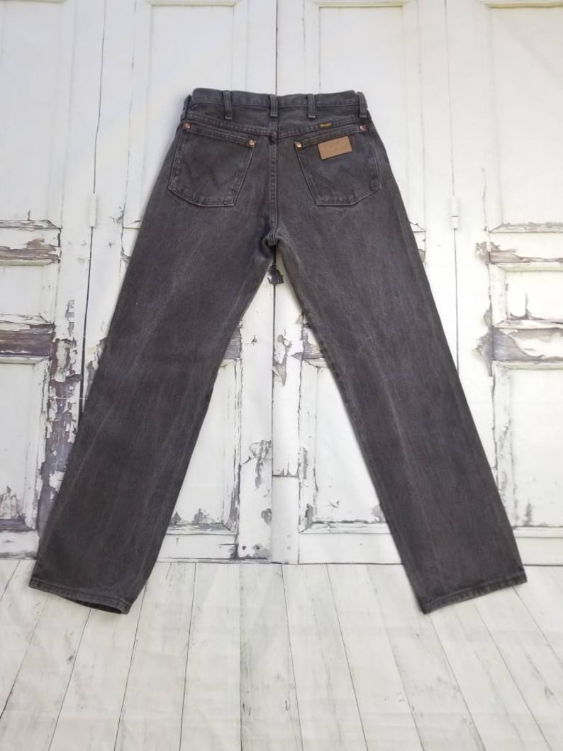 May include: A pair of dark gray denim jeans with a brown leather patch on the back pocket that says "Wrangler".