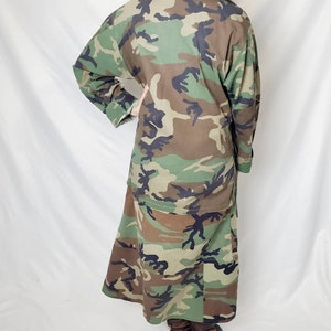 Pode incluir: Casaco comprido com padr&atilde;o de camuflagem em tons de verde, castanho e preto. O casaco tem mangas compridas e uma parte inferior semelhante a uma saia. A pessoa est&aacute; a usar botas castanhas de salto alto. &Eacute; uma pe&ccedil;a de inspira&ccedil;&atilde;o militar.