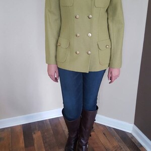 May include: A green double-breasted blazer with gold buttons and flap pockets. The blazer is worn over blue jeans and brown boots.