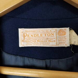 May include: A navy blue Pendleton woolen mills label with white text. The label reads "Warranted to be a Pendleton Trade Mark Reg. U.S. Pat. Off. Pendleton Woolen Mills Portland, Oregon 100% Virgin Wool Pure Virgin Wool Made in U.S.A."