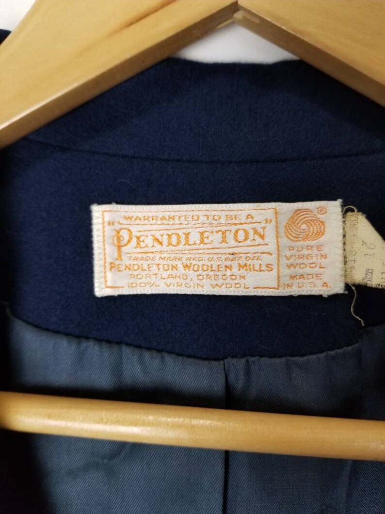 May include: A navy blue Pendleton woolen mills label with white text. The label reads "Warranted to be a Pendleton Trade Mark Reg. U.S. Pat. Off. Pendleton Woolen Mills Portland, Oregon 100% Virgin Wool Pure Virgin Wool Made in U.S.A."