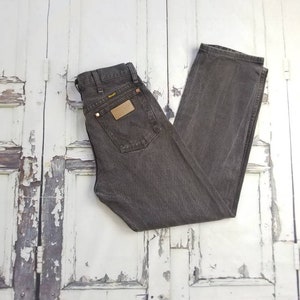 May include: A pair of dark gray denim jeans with a brown leather patch on the back pocket. The jeans have a straight leg and a classic fit.