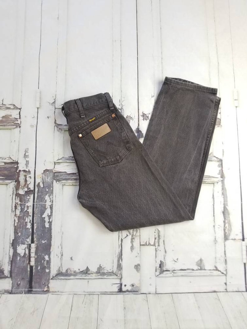 May include: A pair of dark gray denim jeans with a brown leather patch on the back pocket. The jeans have a straight leg and a classic fit.