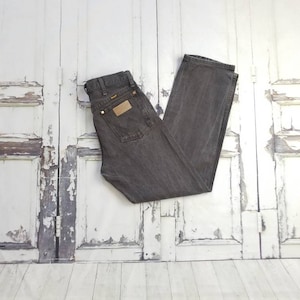May include: A pair of dark gray denim jeans with a brown leather patch on the back pocket. The jeans are folded in half and laid flat on a white wooden surface.