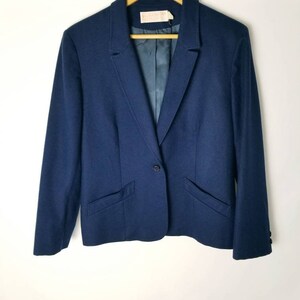 May include: A navy blue blazer with a single button closure and two front pockets. The blazer has a satin lining and is hanging on a wooden hanger.