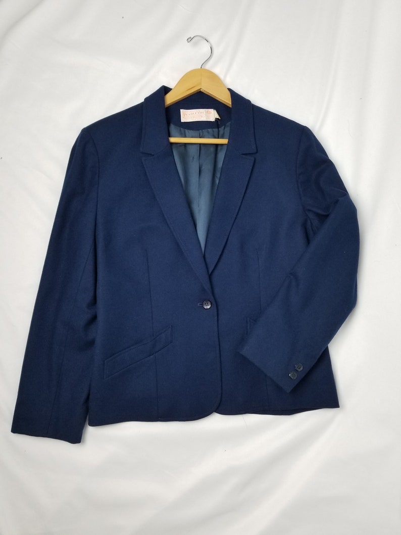 May include: A navy blue blazer with a single button closure and a pocket on the left side. The blazer has a classic, tailored fit.
