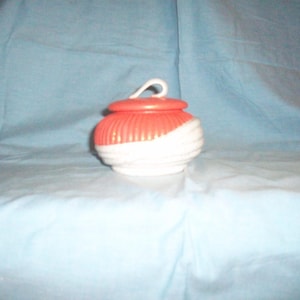 May include: A white and red ceramic jar with a lid and a handle. The jar has a swirl design.