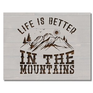 Könnte beinhalten: Ein Holzschild mit weißem Hintergrund und braunem Text, der "Das Leben ist besser in den Bergen" lautet. Das Schild zeigt eine Silhouette von Bergen mit einer Sonne und Bäumen.