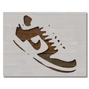 May include: A white stencil of a running shoe on a woodgrain background. The stencil is cut out in the shape of a shoe, with the laces and sole visible.