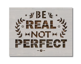 May include: Wooden sign with the message "BE REAL NOT PERFECT" in a stencil font. The sign has a white-washed wood background with brown text and decorative elements like stars, wrenches, and a laurel wreath.