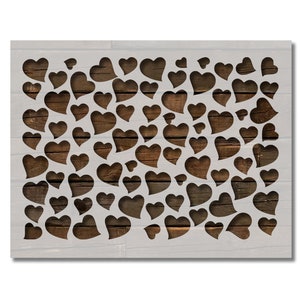 May include: A stencil featuring a pattern of various-sized hearts cut out of a white material. The background reveals a wooden texture, creating a contrast between the shapes and the backdrop. The design is suitable for crafts and decorative projects.