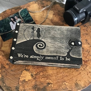 May include: A black wooden photo album with a Nightmare Before Christmas theme. The album features a silhouette of Jack Skellington and Sally, a spiral design, and the text "We're simply meant to be". The album is personalized with the names "Tony & Annalisa" and the date "August 18, 2018".