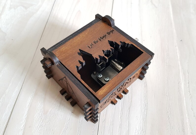 Pu&ograve; includere: Una scatola musicale in legno con una silhouette del castello di Hogwarts e il testo "Let the Magic Begin". La scatola musicale &egrave; marrone con finiture nere.