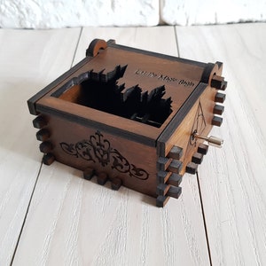 Pu&ograve; includere: Una scatola musicale in legno con un design intagliato di un castello e le parole "Let the Magic Begin". La scatola musicale ha una chiave di carica sul lato.