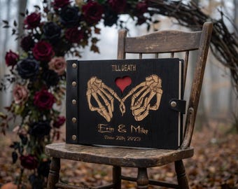 Puede incluir: Un álbum de fotos de madera negra con lomo de postes metálicos. La cubierta presenta un diseño grabado con láser de manos de esqueleto formando un corazón, con el texto "TILL DEATH", "Erin & Mike" y "October 28th 2023" en letras doradas.