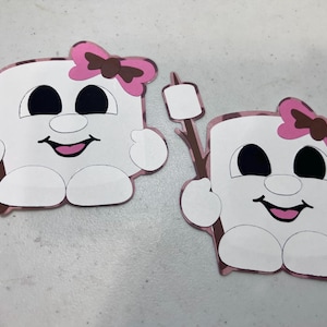 Puede incluir: Dos pegatinas planas troqueladas que muestran un personaje de malvavisco de dibujos animados con cuerpo blanco, ojos negros grandes, boca rosa y un lazo rosa con centro marrón. Cada personaje sostiene un palo marrón con un malvavisco.