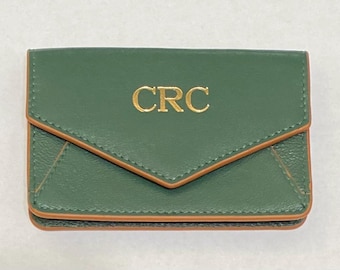May include: A forest green envelope-style card holder featuring a pointed flap and contrasting tan edge piping. The center of the flap is embossed with the gold-colored capital letters CRC. The item has visible stitching along the edges.