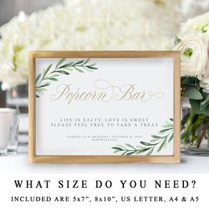 May include: A printable sign for a popcorn bar at a wedding or party. The sign is in a gold frame and features a watercolour design of green leaves and the text "Popcorn Bar". The text below reads "Life is salty, love is sweet. Please feel free to take a treat." The sign also includes the couple's names, wedding date, and hashtag.