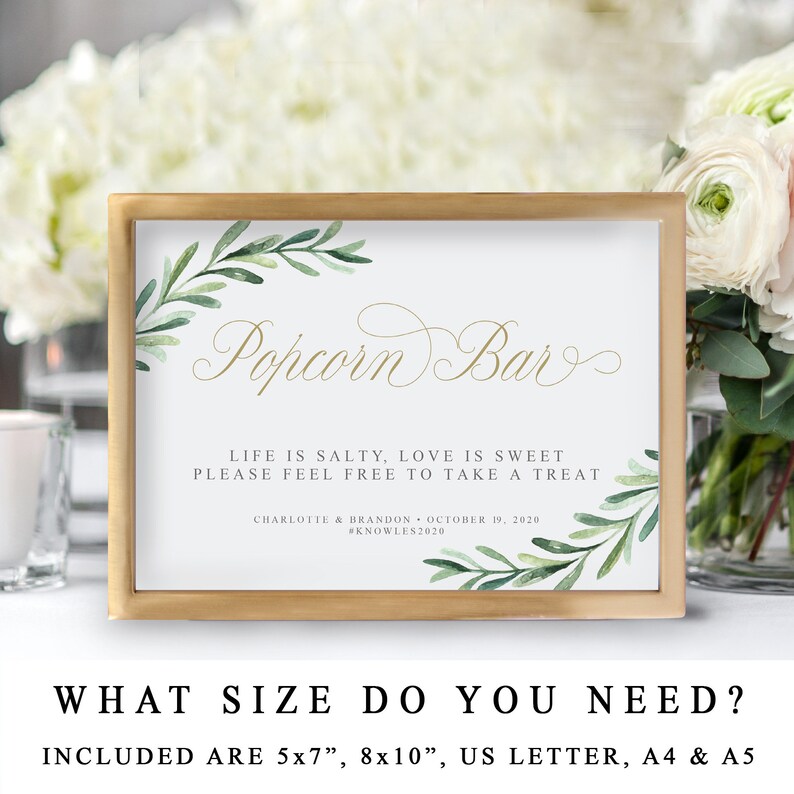 May include: A printable sign for a popcorn bar at a wedding or party. The sign is in a gold frame and features a watercolour design of green leaves and the text "Popcorn Bar". The text below reads "Life is salty, love is sweet. Please feel free to take a treat." The sign also includes the couple's names, wedding date, and hashtag.