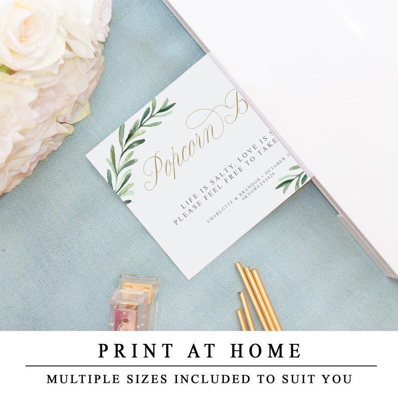 May include: Printable wedding favour sign with green watercolour leaves and gold calligraphy text that reads "Popcorn Bar. Life is salty, love is sweet. Please feel free to take."  The sign also includes the couple's names and wedding date.