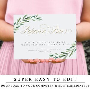 May include: A light blue printable sign with a gold script font that reads "Popcorn Bar". The sign has a watercolour design of green leaves and branches. The text below reads "Life is salty, love is sweet. Please feel free to take a treat." The bottom of the sign includes the names "Charlotte & Brandon" and the date "October 19, 2020" along with the hashtag "#Knowles2020".