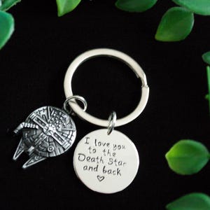 Peut inclure: Porte-clés argenté avec un charme de vaisseau spatial Millennium Falcon et un charme rond avec le texte "Je t'aime jusqu'à l'Étoile de la Mort et retour".