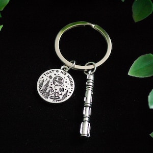 May include: Silver keyring with a round charm that says "That's no moon" and a small lightsaber charm. The charm has a black and white image of the Death Star.
