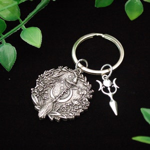May include: Silver charm keychain featuring a crescent moon, a broom, and a pentagram. The charm is surrounded by a floral design.
