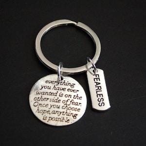 May include: Silver keychain with two charms. One charm has the text "FEARLESS" and the other charm has the text "everything you have ever wanted is on the other side of fear. Once you choose hope, anything is possible."