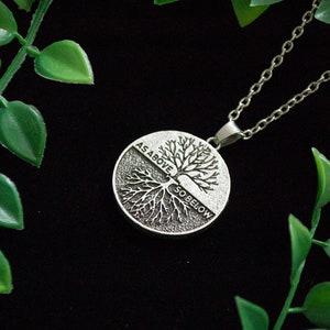May include: A silver necklace with a round pendant featuring a tree with roots and branches. The pendant has the words "As Above So Below" inscribed on it.