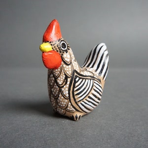 May include: A small ceramic chicken figurine with black and white stripes and a red comb. The chicken is painted with white dots and black lines.