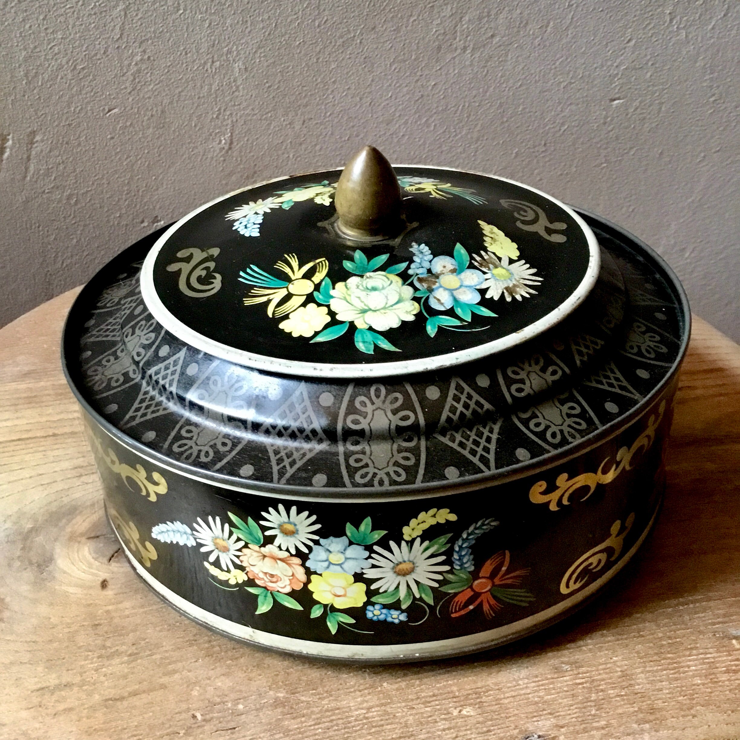 ヴィンテージアンティークの丸型花柄ブリキ缶。黒地に花柄が描かれてい